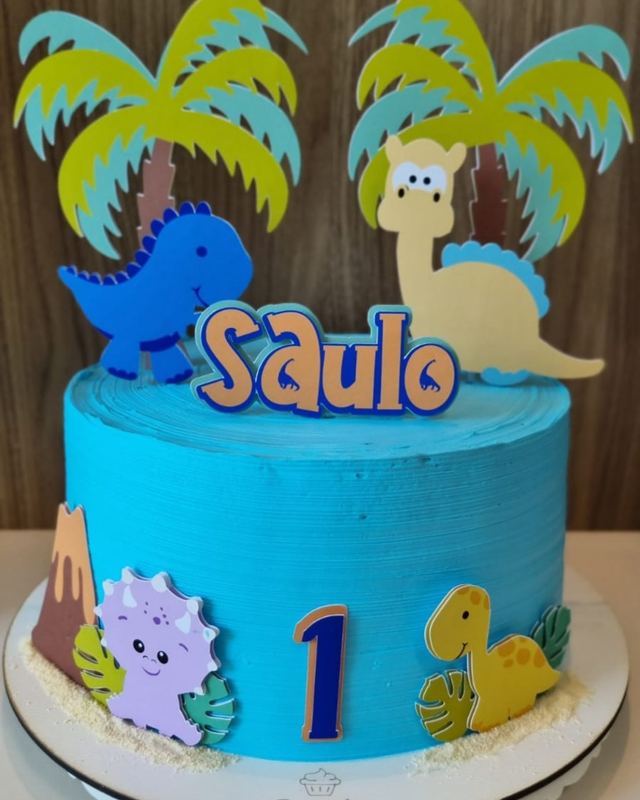 Topo de bolo com dinossauros, coqueiros e o nome Saulo